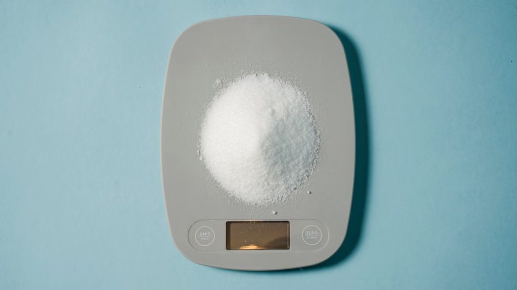 Top view of kitchen scales with electronic display measuring weight of sugar on blue background
